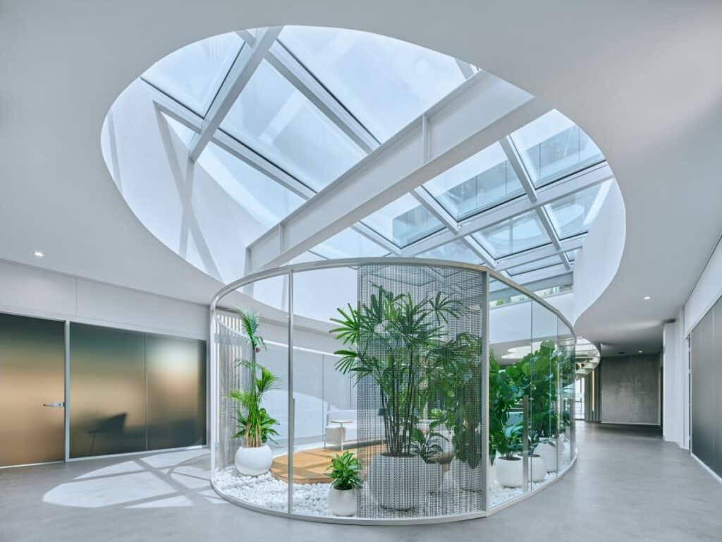 Yüksek tavanlı cam çatılı iç mekan, yeşil bitkilerle donatılmış modern tasarım.